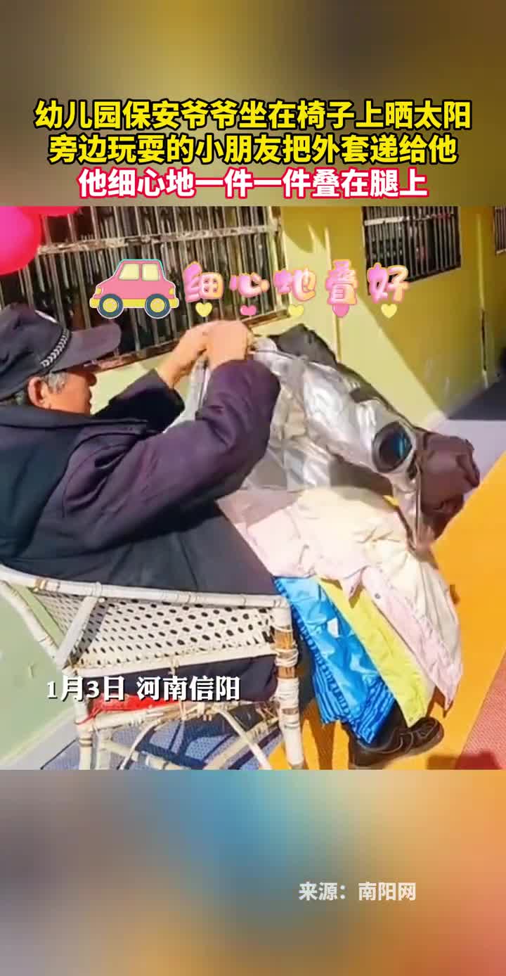 幼儿园保安爷爷坐在椅子上晒太阳旁边玩耍的小朋友把外套递给他他细心地一件一件叠在腿上
