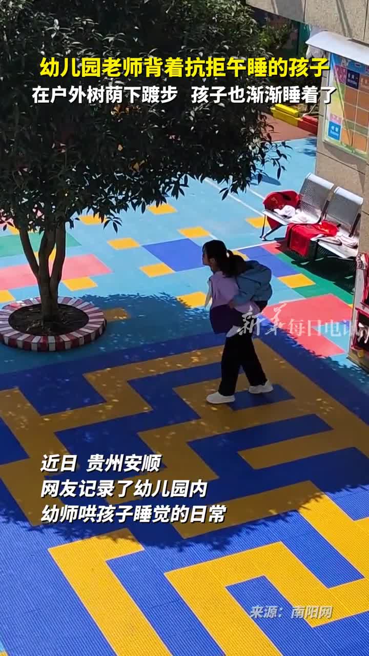幼儿园老师背着抗拒午睡的孩子在户外树荫下踱步孩子也渐渐睡着了