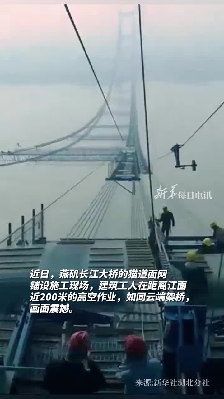 近日燕矶长江大桥的猫道面网铺设施工现场夕阳下建筑工人在距离江面近200米的高空作业伴着脚下的长江波涛仿佛演奏着交响曲
