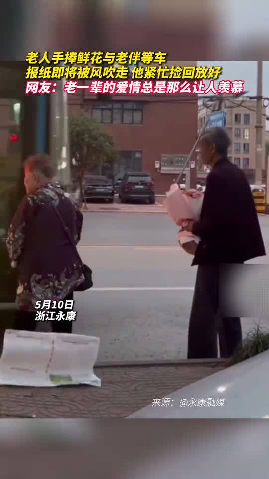 老人手捧鲜花与老伴等车报纸即将被风吹走他紧忙捡回放好网友老一辈的爱情总是那么让人羡慕