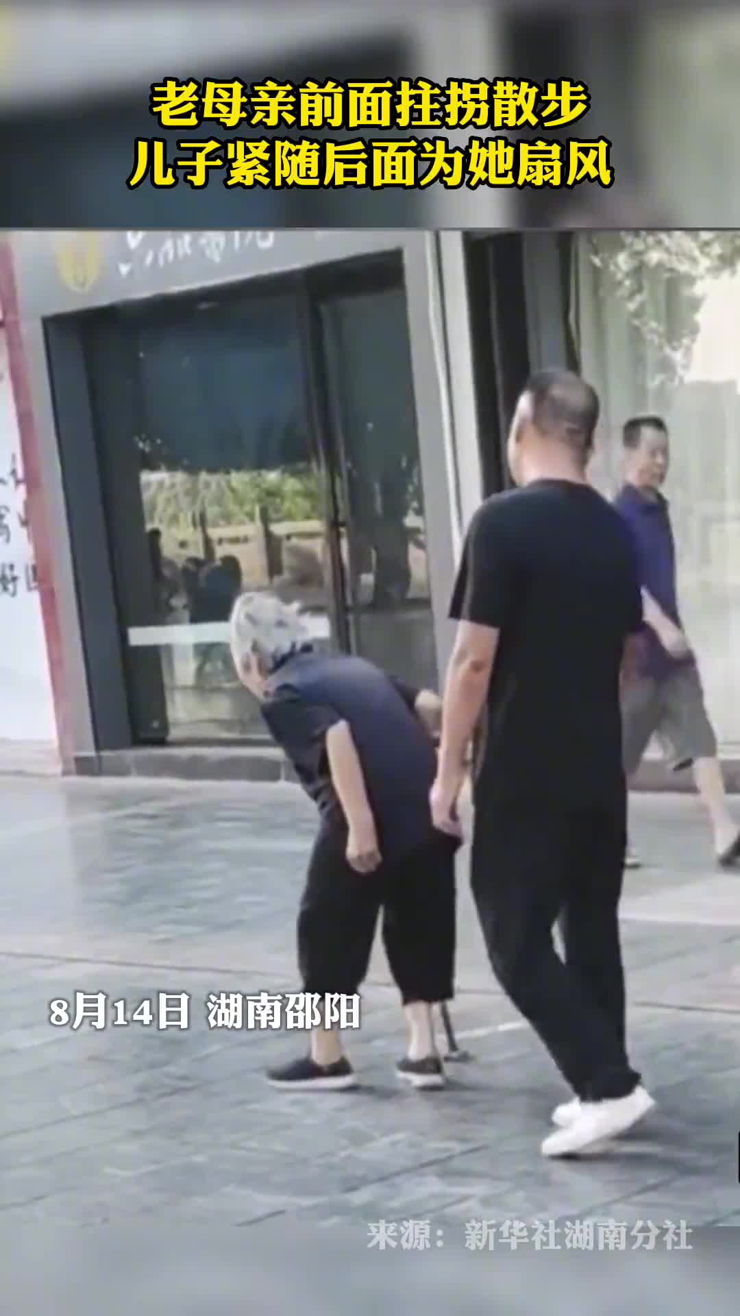 老母亲前面拄拐散步儿子紧随后面为她扇风